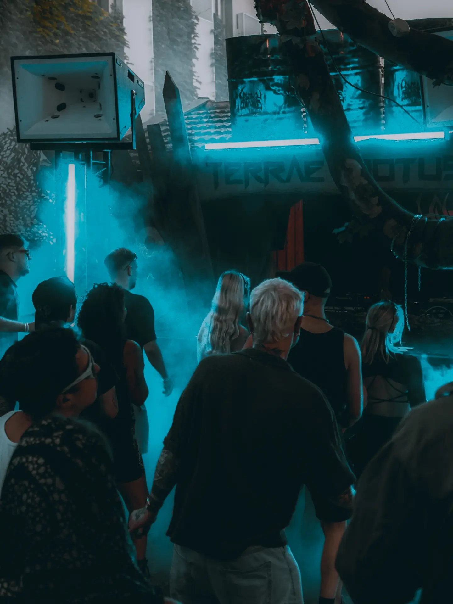 terrae motus open-air-bühne bei nacht — cyan-neon durch nebel, crowd vor dem booth